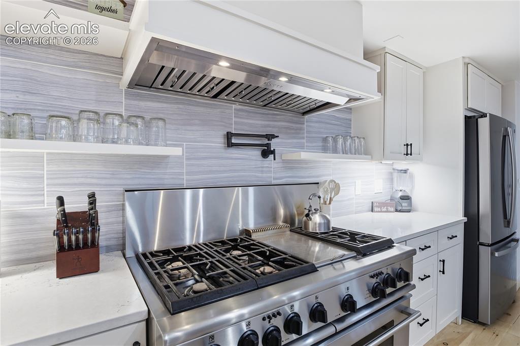 Image 12 of 45: Kitchen, wood floors, sink, stainless steel appliances, custom range hood,