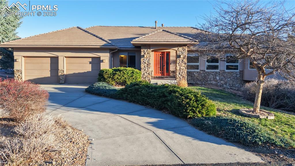 Caption: View of front of property with stone siding, a garage, a tile roof, and concrete driveway