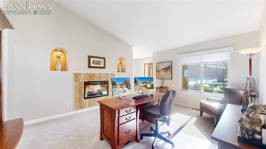 Image 11 of 34: Office area featuring light carpet, a fireplace, baseboards, and high vault
