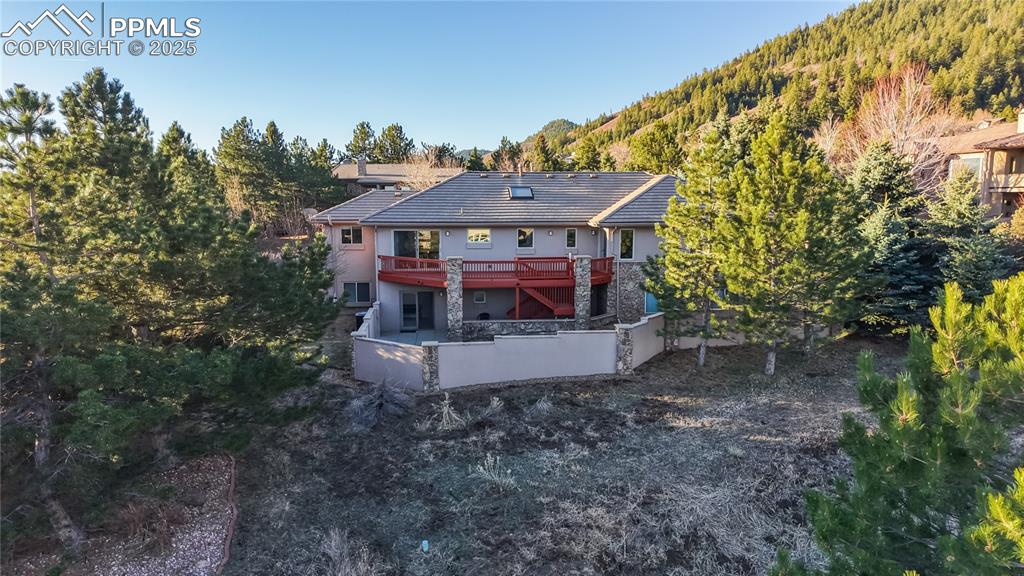 Image 12 of 34: Rear view of property featuring stucco siding, stone siding, a wooded view,