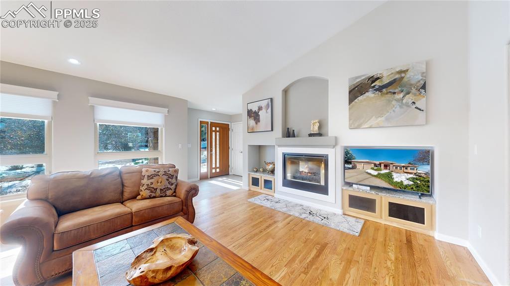 Image 5 of 34: Living area with a multi sided fireplace, wood finished floors, recessed li