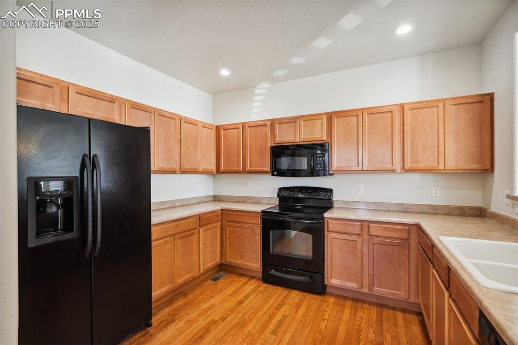 Image 11 of 28: Kitchen featuring black appliances, light wood-style flooring, light counte