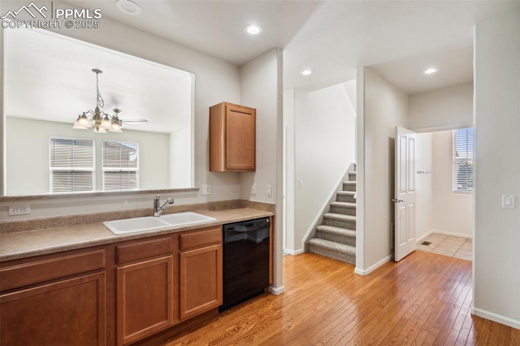 Image 13 of 28: Kitchen with black dishwasher, a chandelier, light wood-style floors, brown