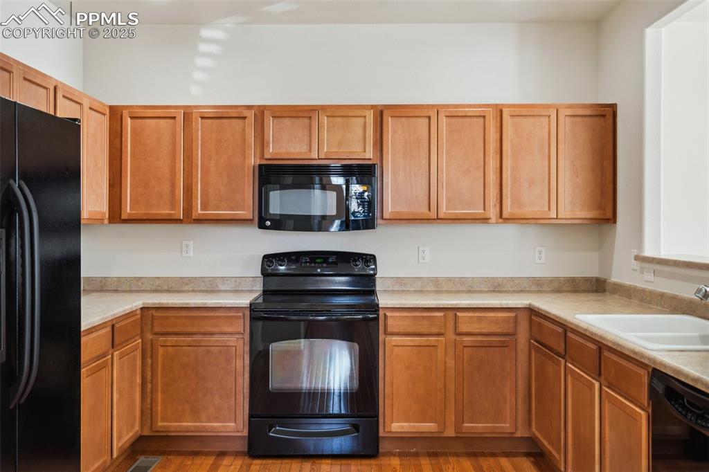 Image 8 of 28: Kitchen featuring black appliances, light countertops, and wood finished fl