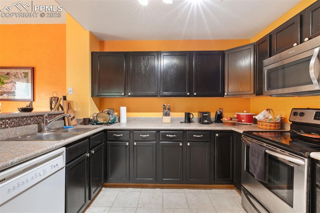 Image 12 of 29: Kitchen with appliances with stainless steel finishes, light countertops, l