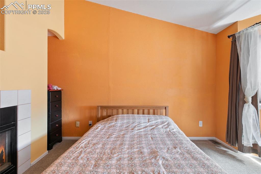 Image 18 of 29: Carpeted bedroom featuring a tile fireplace and baseboards
