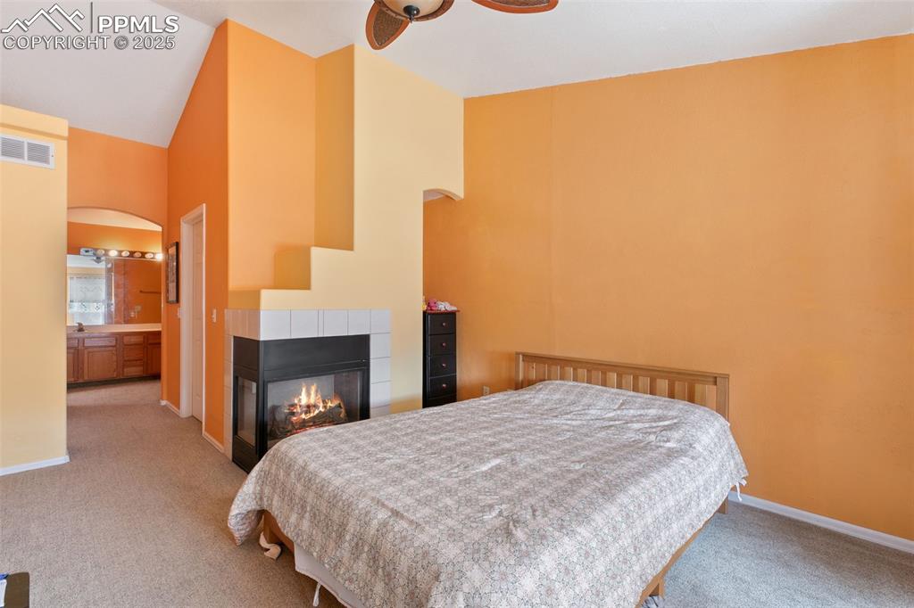 Image 19 of 29: Bedroom featuring high vaulted ceiling, a tile fireplace, light carpet, arc