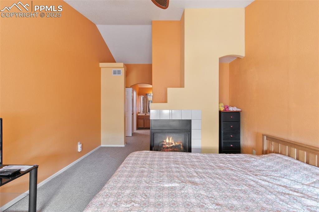 Image 20 of 29: Carpeted bedroom featuring arched walkways, a tile fireplace, and high vaul
