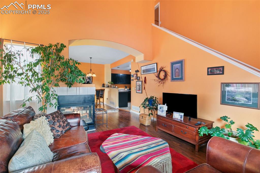 Image 6 of 29: Living area with wood finished floors, a high ceiling, and arched walkways