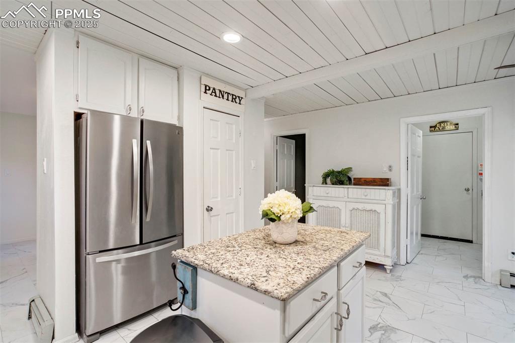 Image 14 of 48: Kitchen with white cabinetry, freestanding refrigerator, light marble finis