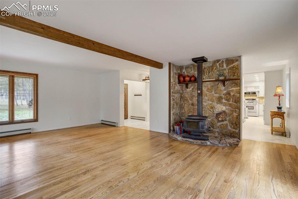 Image 41 of 48: Unfurnished living room with a wood stove, light wood-style flooring, beam 