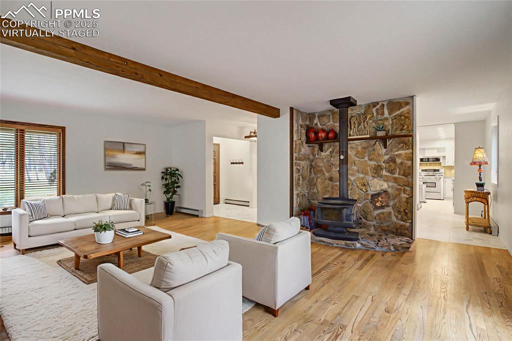 Image 6 of 48: Living room with a wood stove, beamed ceiling, light wood-style floors, a b