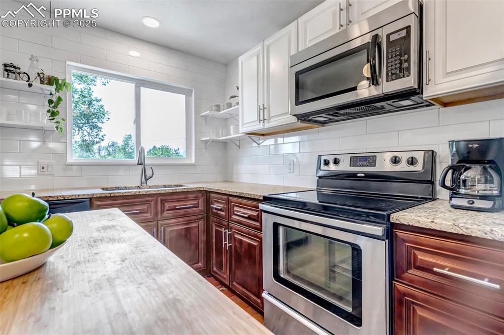 Image 9 of 35: Kitchen featuring stainless steel appliances, open shelves, tasteful backsp