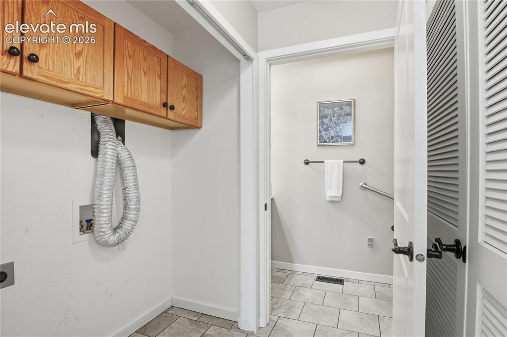 Image 12 of 27: Laundry area featuring wood-finish cabinetry and a tiled floor