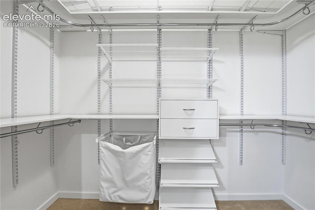 Image 19 of 27: Customizable closet system with white shelving, chrome hanging rods, and bu