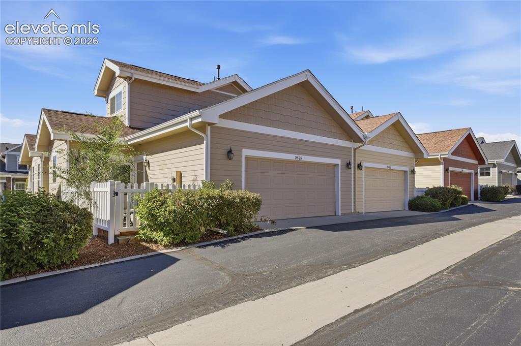 Image 27 of 27: Tan siding with white trim, attached garage, gabled roof, and paved drivewa