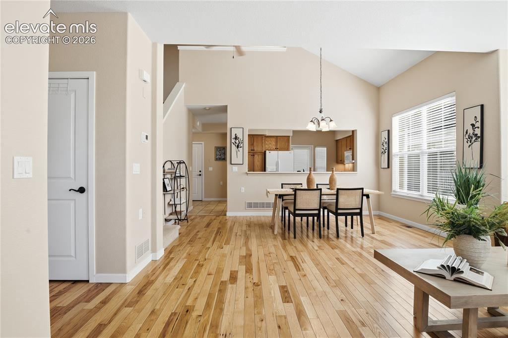 Image 4 of 27: Hardwood flooring, vaulted ceiling, large window with blinds, recessed kitc