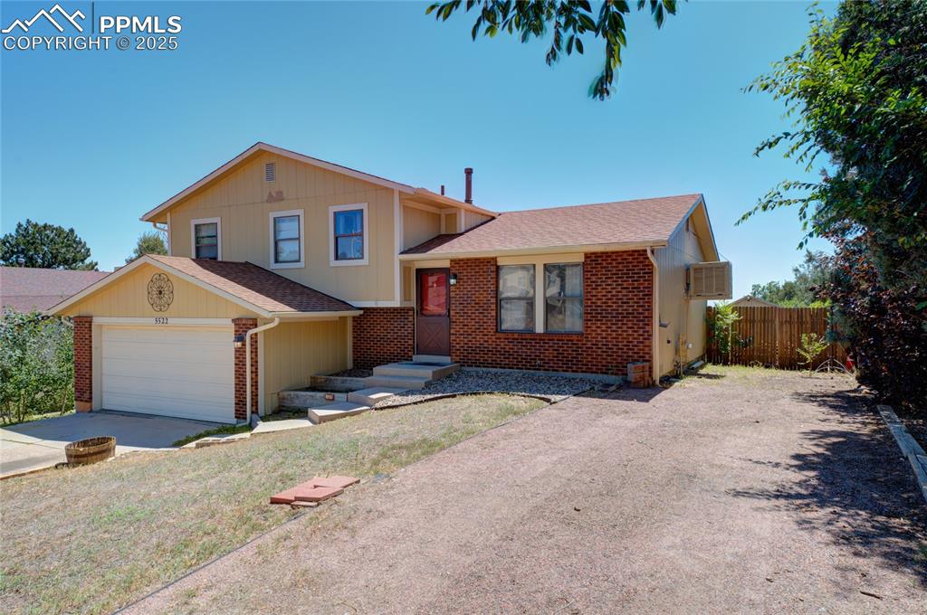Image 2 of 35: Tri-level home with a shingled roof, driveway, brick siding, and an attache
