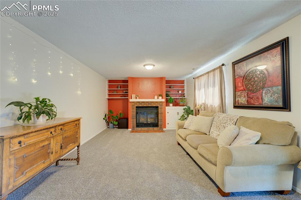 Image 25 of 35: Living area with a textured ceiling, carpet flooring, a fireplace with flus