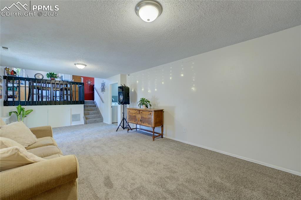 Image 27 of 35: Living area with a textured ceiling, carpet floors, and stairs