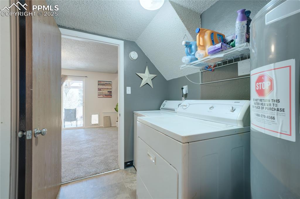 Image 29 of 35: Washroom featuring water heater, a textured ceiling, washer and dryer, and