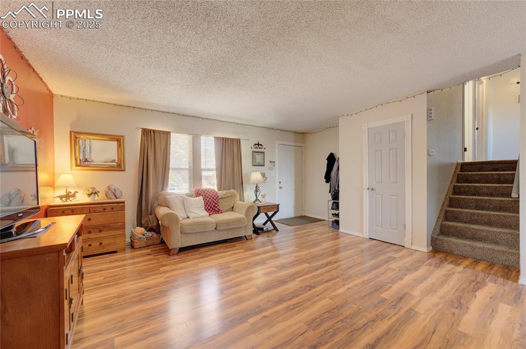 Image 7 of 35: Living area with a textured ceiling, light wood finished floors, and stairw