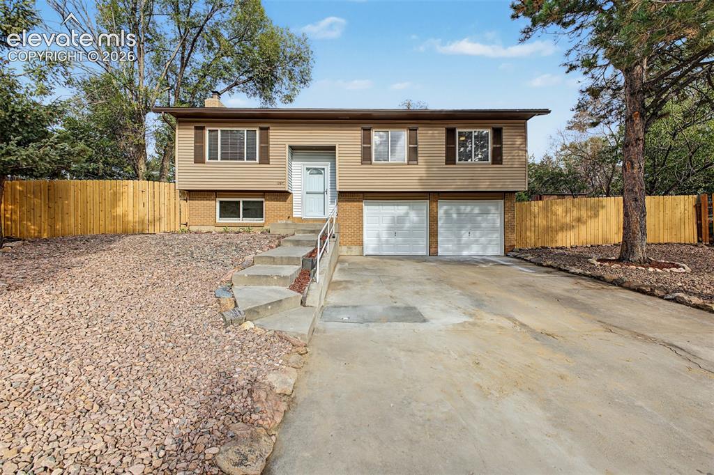 Caption: Two-car garage, split-level architecture, paved driveway, concrete steps with handrail, and a fully 