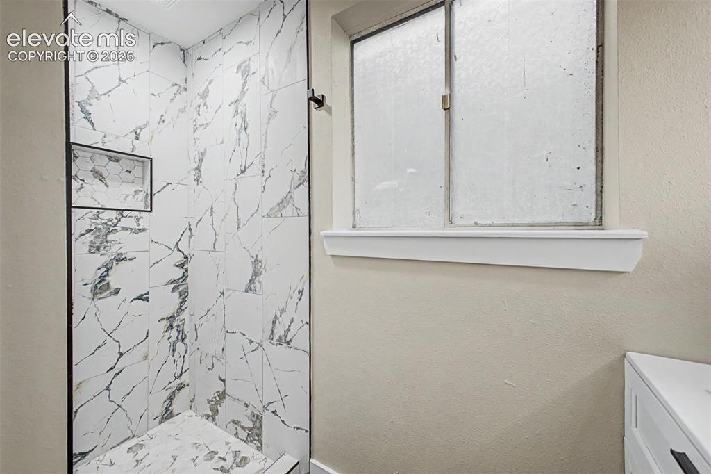 Image 24 of 36: Shower with white and gray veined tile, integrated hexagonal tile niche, an