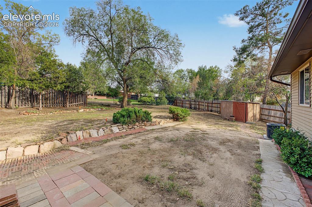 Image 30 of 36: Expansive backyard featuring mature trees, wood fencing, a storage shed, an