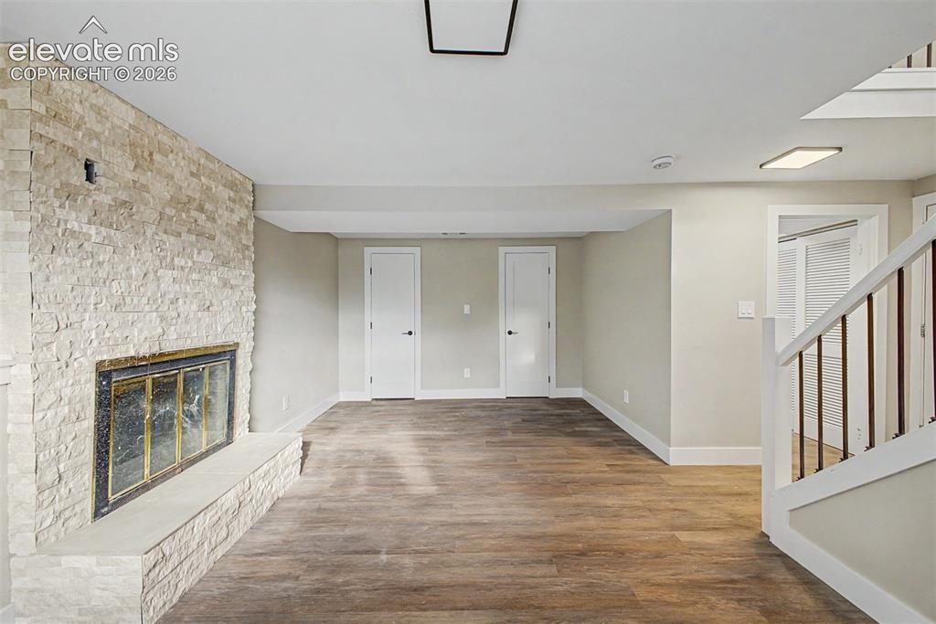Image 4 of 36: Stone-clad fireplace with a hearth, wood-finish flooring, recessed lighting