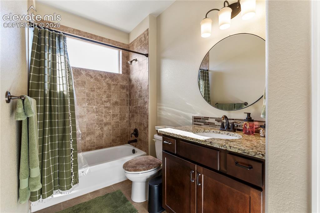 Image 19 of 39: Bathroom featuring a dark wood vanity with stone-finish countertop, round w