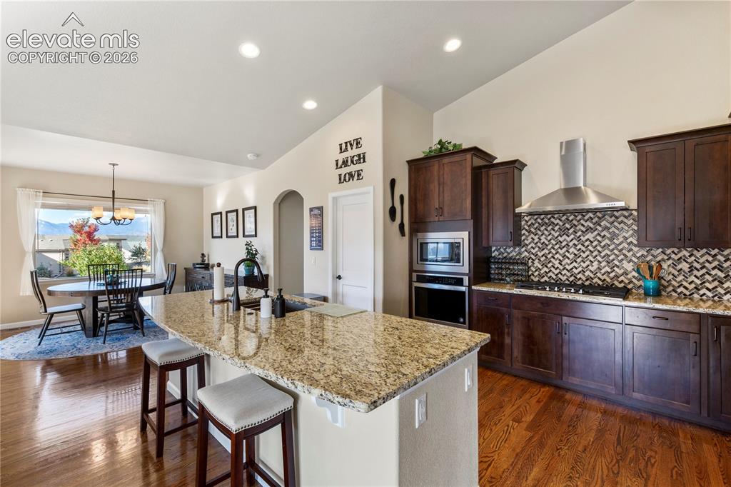 Image 6 of 39: Kitchen featuring dark wood cabinetry, stone countertops, stainless steel w