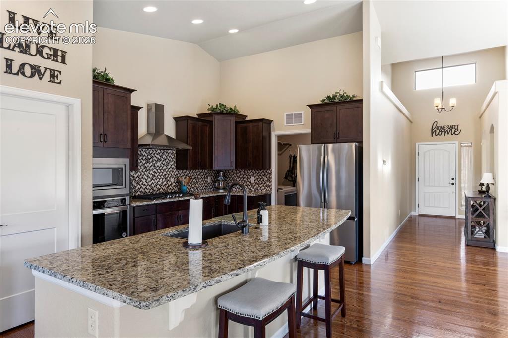 Image 8 of 39: Kitchen featuring high ceilings, stained wood cabinetry, stone countertops,