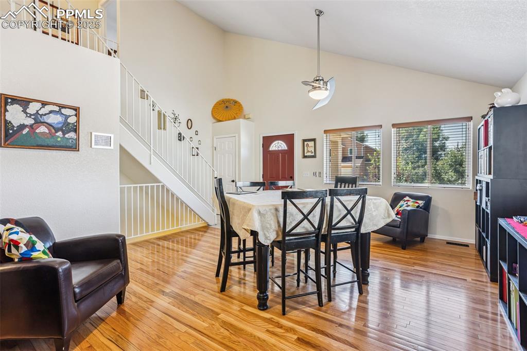 Image 10 of 32: Dining area featuring high vaulted ceiling, wood-type flooring, and stairwa