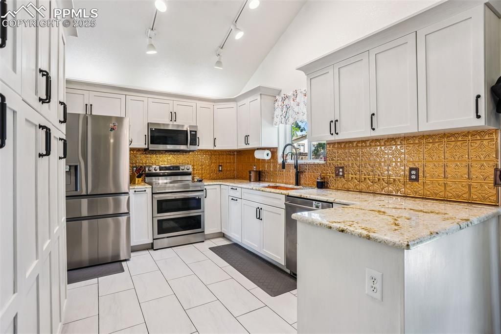 Image 13 of 32: Kitchen with stainless steel appliances, a peninsula, lofted ceiling, light