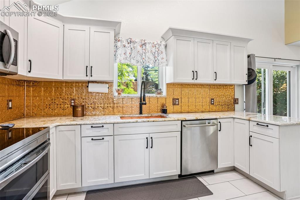 Image 14 of 32: Kitchen with stainless steel appliances, a peninsula, light stone counters,