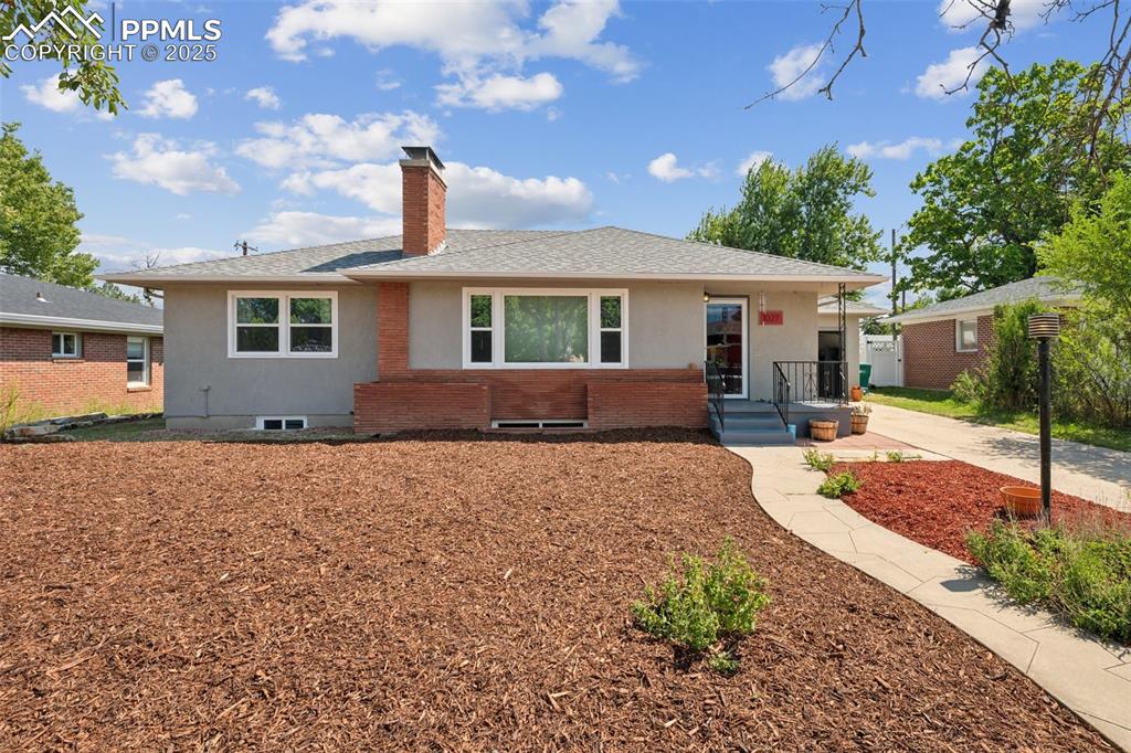 Caption: View of front of home with a chimney, roof with shingles, and brick siding