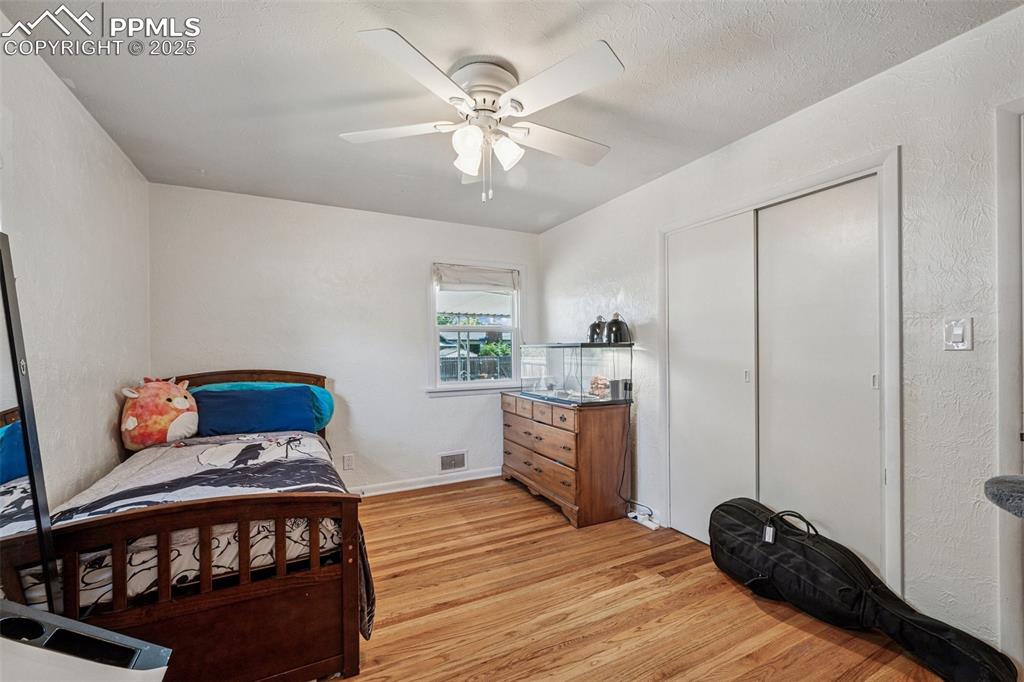 Image 15 of 30: Bedroom with a textured wall, light wood-style floors, a ceiling fan, and a
