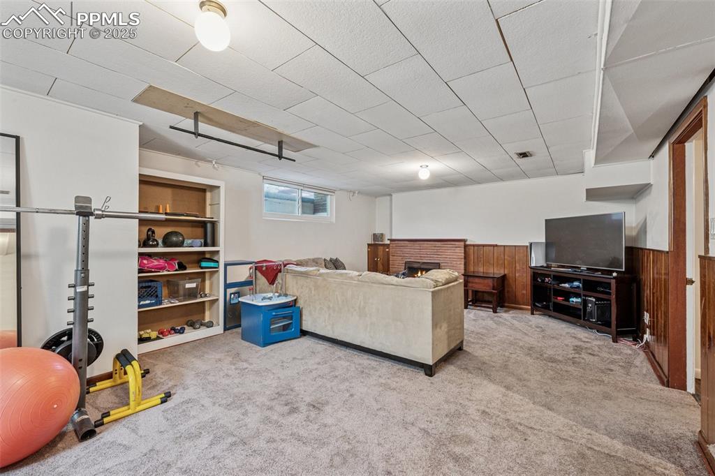 Image 19 of 30: Living area with light carpet, a brick fireplace, wainscoting, and wooden w