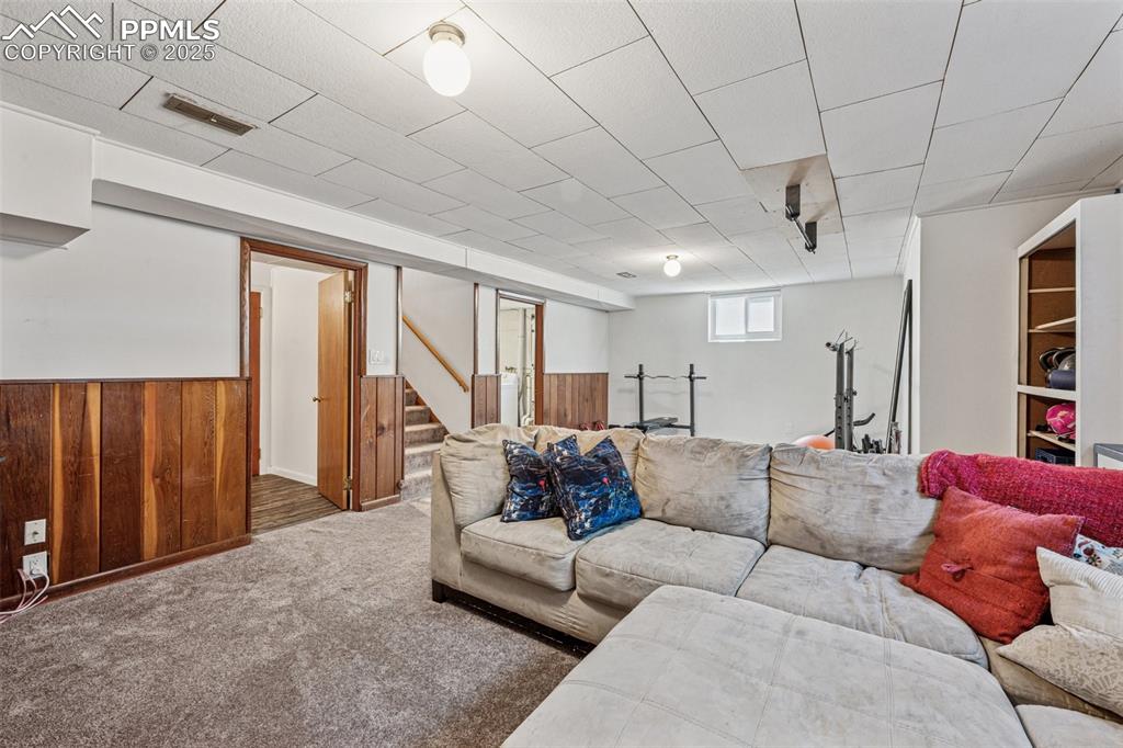 Image 21 of 30: Carpeted living area with wooden walls, stairway, and a wainscoted wall