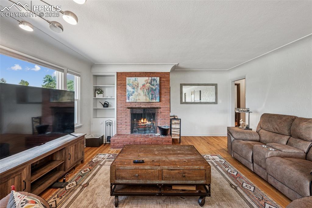 Image 8 of 30: Living room with a fireplace, a textured ceiling, built in shelves, and woo