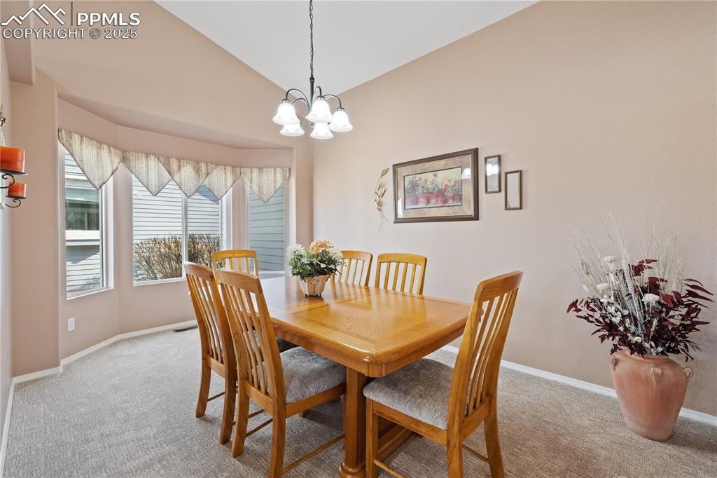 Image 18 of 41: Carpeted dining space with vaulted ceiling and a chandelier