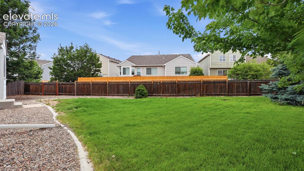 Image 44 of 46: Rear view of home and fenced backyard with mature trees for shade and priva