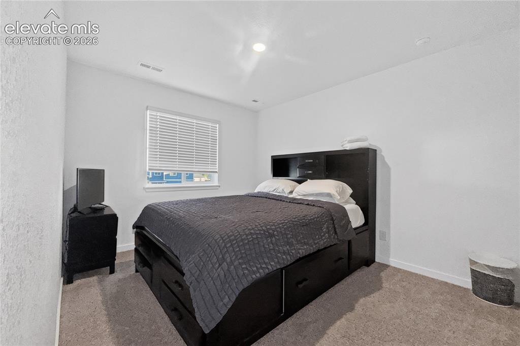 Image 15 of 22: Carpeted bedroom with a window featuring blinds and light-toned walls
