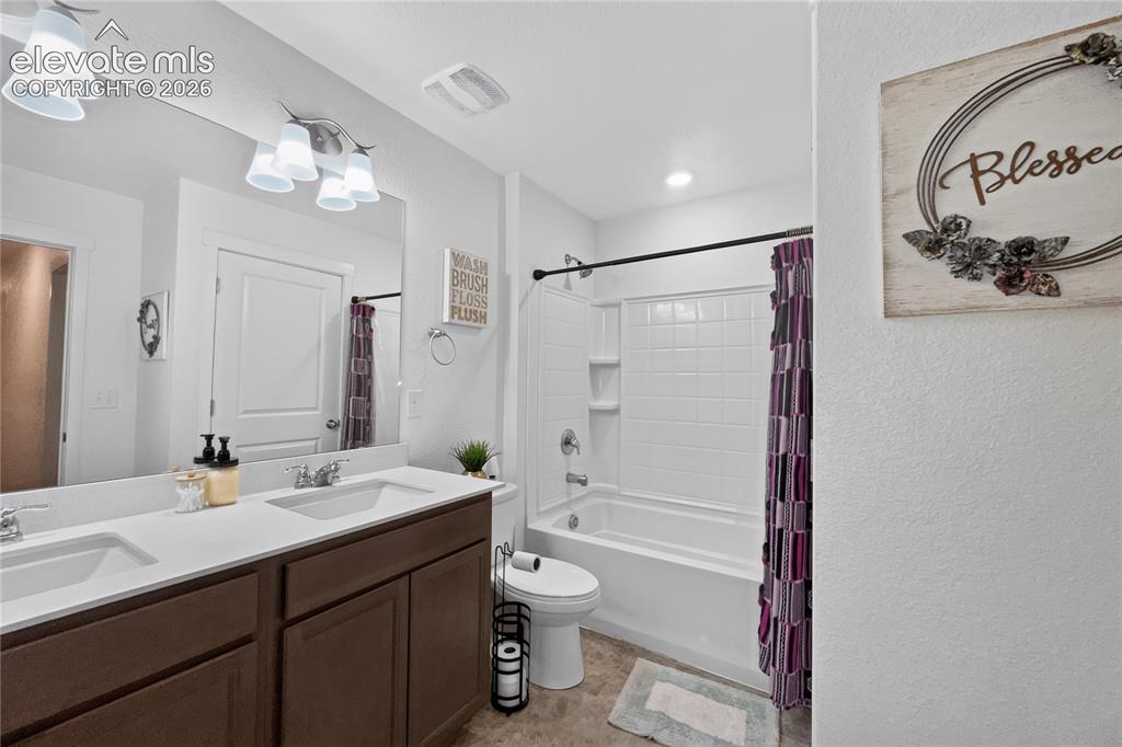 Image 16 of 22: Bathroom featuring a double vanity with brown cabinetry and white counterto