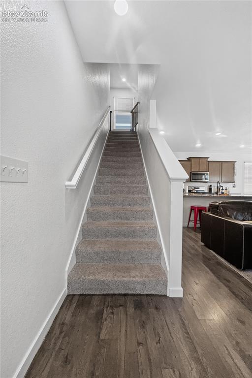 Image 6 of 22: Carpeted staircase with white railings, flanked by wood-finish flooring