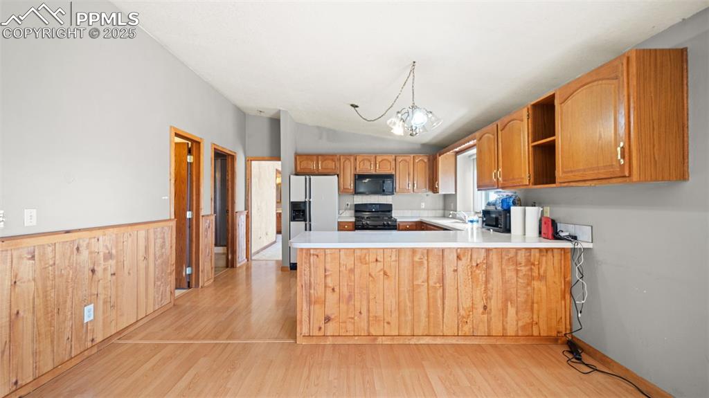 Image 8 of 36: Kitchen featuring black appliances, brown cabinetry, and decorative light f