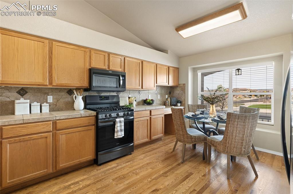 Image 13 of 44: Eat-in kitchen with hardwood floors and tile counters.