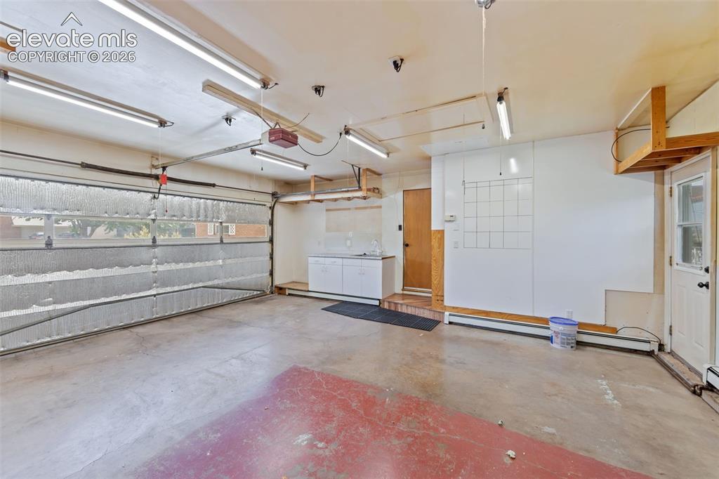Image 21 of 34: Spacious garage featuring an overhead door with frosted panels, multiple fl