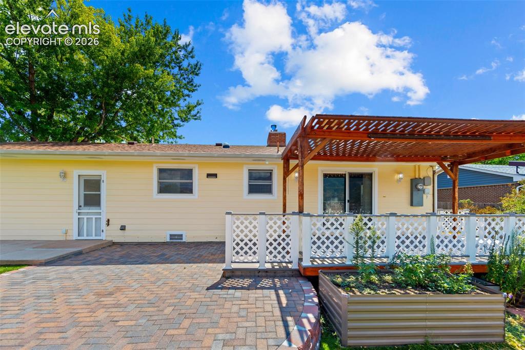 Image 23 of 34: Exterior featuring yellow siding, a spacious brick paver patio, a raised wo